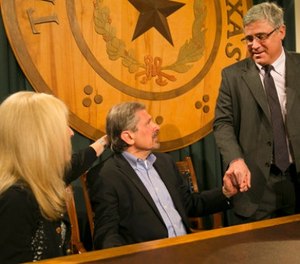 Kent Whitaker, center, reacts to the his lawyer Keith Hampton, right, reading an email from the Texas Board of Pardons and Paroles which voted unanimously to recommend clemency for death row inmate Thomas Whitaker, Kent's son who was found guilty of setting up an ambush that killed his mother and brother in 2003. At left is Kent's wife Tanya, whom he married later. (Ralph Barrera/Austin American-Statesman via AP)