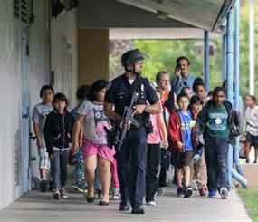 A Santa Monica police officer leads children on a field trip from Citizens of the World Charter School in Los Angeles out of Santa Monica College, where they had gone for a planetarium show, following a shooting in the area.