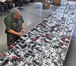 In this April 10, 2009, file photo, Correctional Officer Jose Sandoval inspects one of the more than 2,000 cell phones confiscated from inmates at California State Prison, Solano in Vacaville, Calif. (AP Photo/Rich Pedroncelli, File)