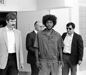 In this July 31, 1983, file photo, Kevin Cooper, center, a suspect in connection with the slashing death of four people in Chino, is escorted to a car for transport to San Bernadino from Santa Barbara, Calif., after he was arrested by police at Santa Cruz Island.