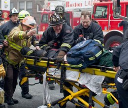 Firefighters and emergency medical personnel rush a firefighter from the scene of a multi-alarm fire at a four-story brownstone in the Back Bay neighborhood near the Charles River, Wednesday, March 26, 2014, in Boston. (AP Photo/Scott Eisen)