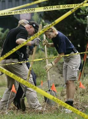 In this 2007 photo, police tape is seen in the foreground as investigators use shovels to examine a field near the home of Christy Freeman, 37, who was charged with first-degree murder in the death of her newborn baby. The bodies of four small infants were found at the home of a Freeman who denied having been pregnant, even after she was taken to a hospital and doctors discovered a placenta and part of an umbilical cord, police said. (AP Photo/Matt Rourke) 
