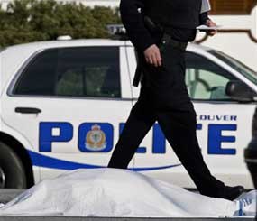 A police officer walks past a body covered by a blanket following a suspected shooting in Vancouver, British Columbia, in February 2009. (AP Photo)