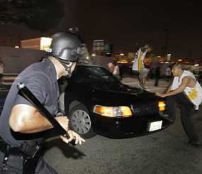 A police officer chases away two men vandalizing a police vehicle in Los Angeles after the Los Angeles Lakers defeated the Orlando Magic to win the NBA championship. (AP Photo/Jae C. Hong)