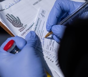 A registered nurse works on filling out vaccine cards while holding a vial of the Moderna COVID-19 vaccine.