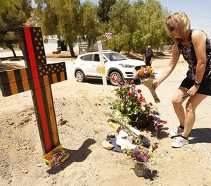 Cindee Erdman places flowers at a memorial featuring a cross made of wood along with flowers located outside Los Angeles County Fire Dept. Station 81 where LA County Firefighter specialist Tory Carlon was killed in a shooting.