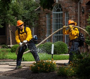 A firefighter sprays an area labeled "fire" during a simulated wildfire exercise in the Jester Estates neighborhood in West Austin on Tuesday. The program is one of the first in the country to focus on urban interface firefighting.