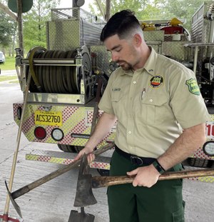 Peter Scalco, a Florida Forest Service wildfire firefighter, holds up the hand tools he used to cut lines around a 35,000-acre fire in Montana.