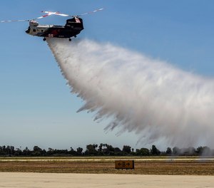 A Boeing CH-47 Chinook helitanker dumps 3,000 gallons of water during a demonstration at the Los Alamitos Joint Forces Training Base in Los Alamitos, Calif., on June 14, 2021. Two of this model of aircraft are part of the regional Quick Reaction Force, which was formed through a partnership among Southern California Edison, the Orange County Fire Authority, and the fire departments of Los Angeles and Ventura counties.