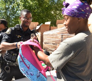 St. Paul Police Officer Lorenzo Lamb hands a backpack to Demetria Smith at the second annual Barbers & Backpacks event.