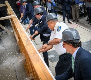 Officials including Baltimore Police Commissioner Michael Harrison use sledge hammers on a ceremonial wall to launch Guardian House.