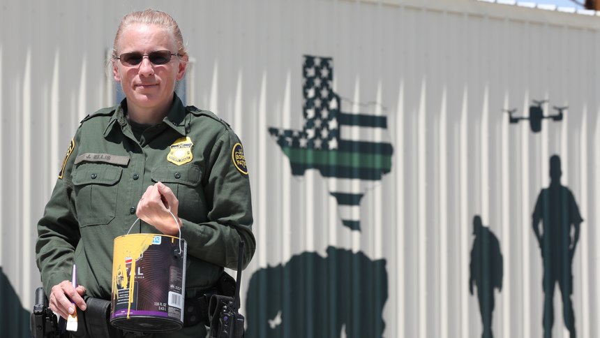 Border Patrol Watch Commander Janenne Ellis poses with some of the paint supplies used in the mural behind her at the Presidio Border Patrol Station in Presidio, Texas.