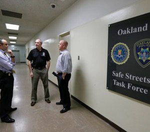 In this Friday, March 10, 2017, photo, from left Russell Nimmo, FBI supervisory special agent, and FBI agent Paul Healy talk with Oakland police detective Brad Baker outside the offices of the Oakland Safe Streets Task Force in Oakland, Calif.