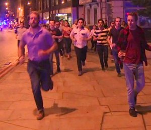 In this image taken from video footage, people run from the scene of attack, alongside a man strolling holding a pint of beer, right, in London, late Saturday, June 3, 2017.