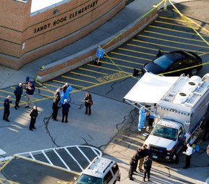 In this Dec. 14, 2012, file photo, officials stand outside of Sandy Hook Elementary School after a shooting in Newtown, Conn.