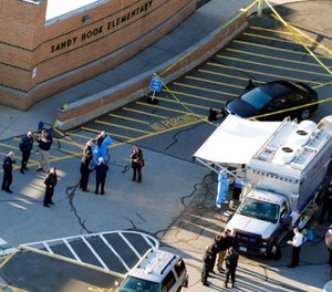 In this Dec. 14, 2012, file photo, officials stand outside of Sandy Hook Elementary School after a shooting in Newtown, Conn.