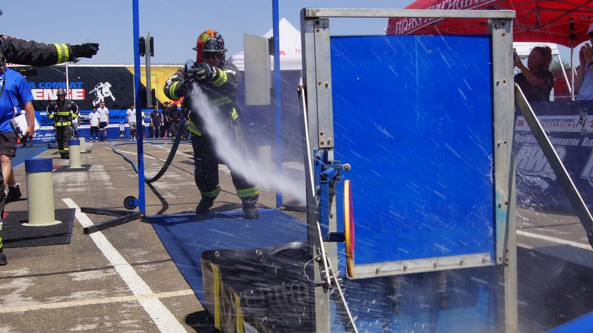 Competitors pick up the nozzle end of the charged hoseline and advance it 75 feet through the swinging “saloon door” at the other end of the course.