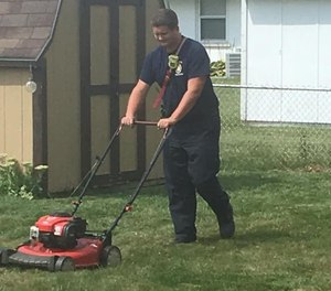 Firefighter mows the lawn of a homeowner.