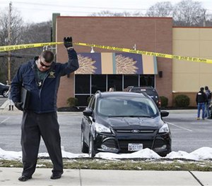 An investigator walks beneath a police tape line at the scene of a shooting at a shopping center in Abingdon, Md., Wednesday, Feb. 10, 2016.