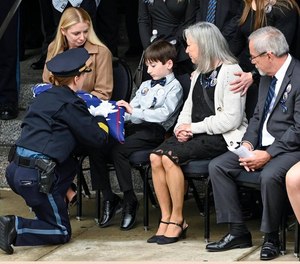 Kansas City Police Chief Stacey Graves, left, presents a flag to Ayden, a son of fallen Kansas City Police Officer James Muhlbauer, 42, during the funeral for Muhlbauer and his police K-9, Champ, Wednesday, Feb. 22, 2023, at Municipal Auditorium in Kansas City. Muhlbauer s family, including his wife, Cassie, left, looks on.