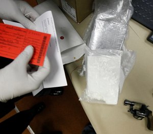 A narcotics officer tags cocaine, a handgun and cash as evidence after being shown at a news conference at police headquarters in Detroit.