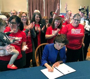 Cheers erupt as Rhode Island Gov. Gina Raimondo signs an executive order Monday, Feb. 26, 2018, in Warwick, R.I., to establish a new policy to try to keep guns away from people who show warning signs of violence.