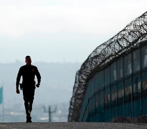In this June 22, 2016 file photo, Border Patrol agent Eduardo Olmos walks near the secondary fence separating Tijuana, Mexico, background, and San Diego in San Diego. (AP Photo/Gregory Bull, File)