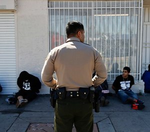In this March 15, 2018 photo, a Los Angeles County Sheriff's deputy keeps watch on a group of people apprehended at an illegal marijuana dispensary in Compton, Calif. The number of outlaw dispensaries in the county greatly outnumbers the about 150 licensed storefront retailers. (AP Photo/Jae C. Hong)