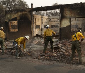 Fire crews clear rubble from the road near a building burned in the Camp Fire, Monday, Nov. 12, 2018, in Paradise, Calif.