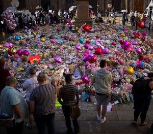 People stand near tributes placed in St. Ann's Square in Manchester, England, after a terrorist bombing in 2017 that killed 22 people attending an Ariana Grande concert. A court heard during an inquiry into the response to the bombing that only one paramedic was on the scene within the first 40 minutes after the bombing.