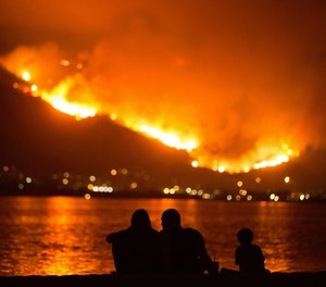 In this Aug. 9, 2018, file photo, a family sits along the shore of Lake Elsinore as they watch the Holy Fire burn in the distance in Lake Elsinore, Calif. The National Interagency Fire Center is predicting a heavy wildfire season for areas along the west coast of the United States this summer. The Boise, Idaho-based center said Wednesday, May 1, 2019, that most of the country can expect a normal wildfire season in the period from May through August. (AP Photo/Patrick Record, File)