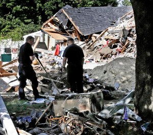 Fire investigators pause while searching the debris at a home which exploded following a gas line failure in Lawrence, Mass.