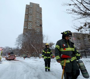 Minneapolis firefighters leave after a deadly fire at a high-rise apartment building, in background.