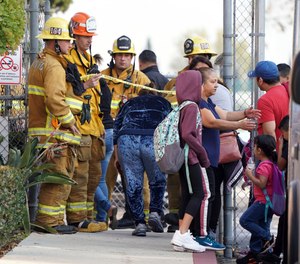 Firefighters allow parents into Park Avenue Elementary School where multiple people were treated for jet fuel exposure in Cudahy, Calif., on Tuesday, Jan. 14, 2020. A jet returning to LAX dumped its fuel over the neighborhood and the school. Affected people at the school were treated for skin and eye irritation. No patients were transported to hospitals.