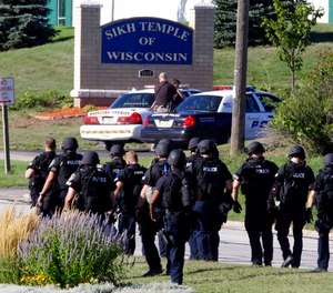 In this Aug. 5, 2012 photo, police walk near the Sikh Temple of Wisconsin in Oak Creek, Wis., after an active shooter killed six people.