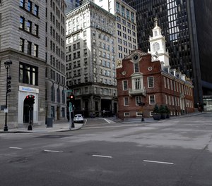 A passer-by walks through a nearly empty intersection near the Old State House, right, in downtown Boston, Tuesday, March 24, 2020.