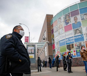 An NYPD officer wears personal protective equipment while maintaining order along a line to enter COVID-19 testing site at Elmhurst Hospital Center, Wednesday, March 25, 2020, in New York. (AP Photo/John Minchillo)