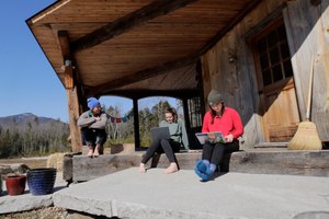 Ashley Bullard, left, sits on the porch of her family's rural home in North Sandwich, N.H., as her daughters Raven, center, a senior in high school, and Willow, right, a freshman at Brandeis University, try to complete their classwork from home during the virus outbreak on a very limited internet connection. Image: AP Photo/Charles Krupa