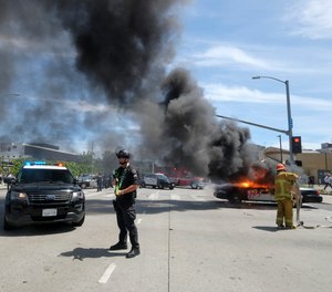 A police officer stands guard as a firefighter extinguishes a burning police vehicle during a protest over the death of George Floyd in Los Angeles, Saturday, May 30, 2020.