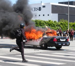 A person runs while a police vehicle is burning during a protest over the death of George Floyd in Los Angeles, Saturday, May 30, 2020. (AP Photo/Ringo H.W. Chiu)