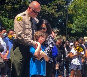 Santa Cruz Sheriff Jim Hart stands next to fallen Sgt. Damon Gutzwiller's pregnant widow and child, as more than a thousand people gather outside the Santa Cruz County Sheriff-Coroner's Office to pay their respects in Santa Cruz, Calif., Sunday, June 7, 2020. (AP Photo/Martha Mendoza)