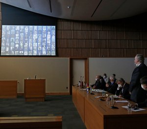 The photos of the 84 people killed in the 2018 Camp Fire are displayed as Bill Johnson, CEO and president of PG&E Corp., right, stands as the charges are read against the company's action that caused the fire.