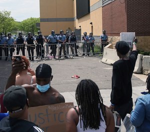 In this May 27, 2020, file photo, a protester holds a newspaper in front of the Minneapolis police standing guard against protesters at the Third Precinct as people protest the arrest and death of George Floyd.