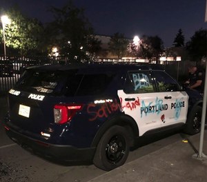 An officer stands near a vandalized Portland Police vehicle on Saturday, July 18, 2020, in Portland, Ore.