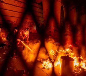 A protester extinguishes a fire set by fellow protesters at the Mark O. Hatfield United States Courthouse on Wednesday, July 22, 2020, in Portland, Ore.