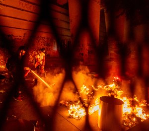 A protester extinguishes a fire set by fellow protesters at the Mark O. Hatfield United States Courthouse on Wednesday, July 22, 2020, in Portland, Ore.