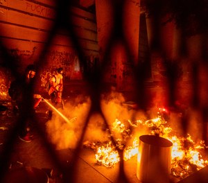 A protester extinguishes a fire set by fellow protesters at the Mark O. Hatfield United States Courthouse on Wednesday, July 22, 2020, in Portland, Ore.