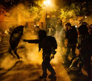 Protesters walk through chemical irritants dispersed by federal agents at the Mark O. Hatfield United States Courthouse on Thursday, July 23, 2020, in Portland, Ore. (AP Photo/Noah Berger)