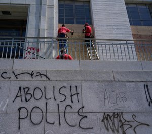 Workers place wooden boards over windows as graffiti is shown on walls at the Alameda County Courthouse in Oakland, Calif., Sunday, July 26, 2020.