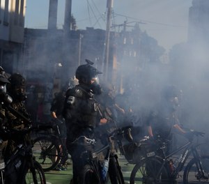 Seattle police officers wear gas masks and carry weapons as smoke rises and they clash with protesters, Saturday, July 25, 2020, in Seattle.